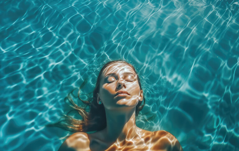 High angle view of woman relaxing in the swimming pool under clear blue water with closed eyes. Female face out of water, summer vacation concept.